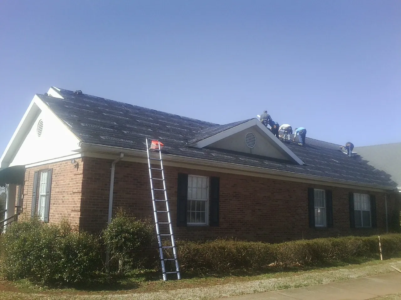 Crew tearing shingles off a brick ranch roof with a ladder set — Metal Roof Repair work by our crew in Carrolls
