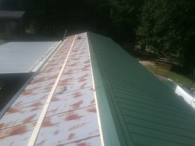 Old rusted panels beside newly installed green metal roofing — Wind Damage Roof Repair by Roofing Brothers in Carrolls