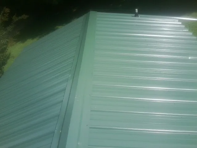 New green metal panels meeting at the ridge of a roof — Flat Roof Repair work by our crew in Carrolls