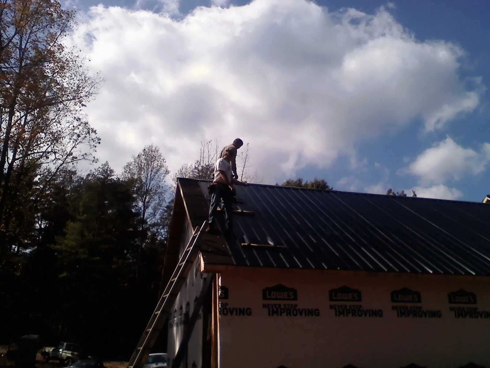 Roofer fastening dark metal panels high against a cloudy sky, from a Roof Inspection job in Carrolls