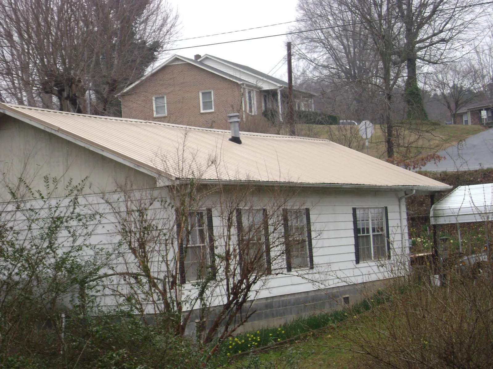 Tan metal roof on a white sided house set into a hillside — Commercial Roofing by Roofing Brothers in Carrolls